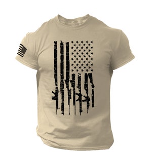 May include: A tan t-shirt with a black and white American flag design. The flag is made up of guns instead of stripes.