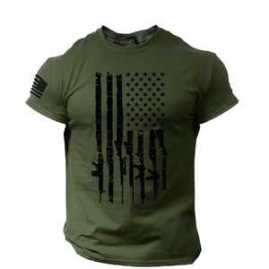 May include: A green short-sleeved t-shirt with a black distressed American flag design. The flag is made up of guns instead of stripes.