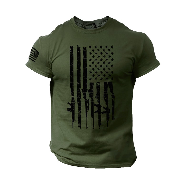 May include: A green short-sleeved t-shirt with a black distressed American flag design. The flag is made up of guns instead of stripes.