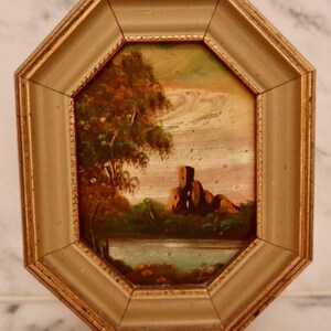 May include: A framed painting of a landscape with a stone building in the distance. The painting is in a gold octagonal frame.