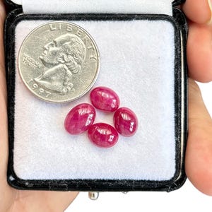 May include: Five oval-shaped, red gemstones in a small, black velvet jewellery box. The gemstones are approximately the size of a UK 20 pence coin.
