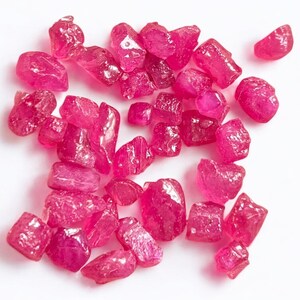 May include: A collection of loose pink ruby gemstones. The rubies are various sizes and shapes, with some having a more polished look than others.