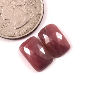 Può includere: Due pietre preziose di zaffiro rosa sfaccettate, ciascuna di forma rettangolare, sono mostrate accanto a un quarto di dollaro americano per il confronto delle dimensioni.