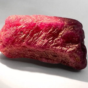 Może przedstawiać: Duży, surowy, czerwony rubin. Rubin ma intensywny czerwony kolor i fakturowaną powierzchnię.