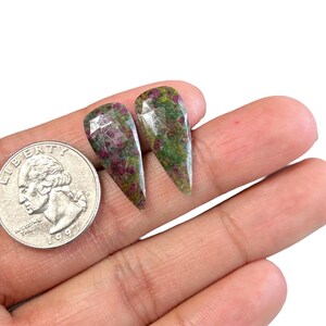 Könnte beinhalten: Zwei grüne, rosafarbene und weiße Edelsteinkabochons in Tropfenform. Die Edelsteine sind etwa so groß wie eine deutsche 2-Euro-Münze.