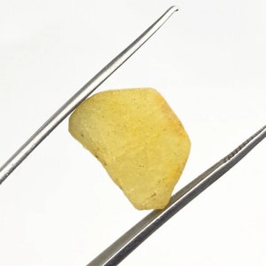 May include: A yellow, translucent, irregularly shaped gemstone held by tweezers.