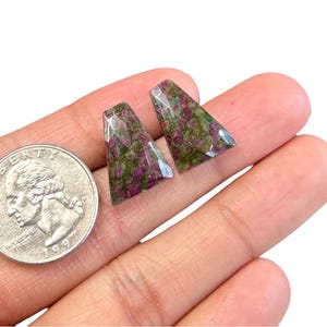 May include: Two triangular shaped green and pink gemstone cabochons with a silver backing. The gemstones are approximately 2.5 cm in length.