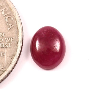 May include: A deep red oval cabochon gemstone, approximately the size of a UK 20 pence coin.