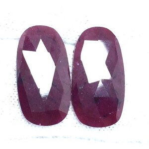 Pode incluir: Duas pedras preciosas de forma oval, facetadas, de cor vermelho escuro com um corte em forma de estrela no centro.