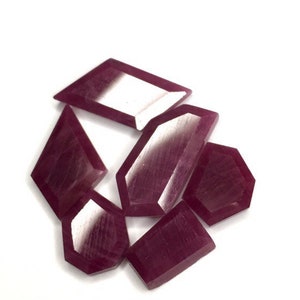 Puede incluir: Un grupo de seis pequeñas piedras preciosas de color púrpura facetadas. Las piedras preciosas tienen varias formas, incluyendo un hexágono, un diamante y un rectángulo.