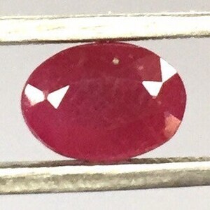 Puede incluir: Primer plano de una piedra preciosa ovalada roja con inclusiones blancas. La piedra preciosa está engastada en un engaste de plata.