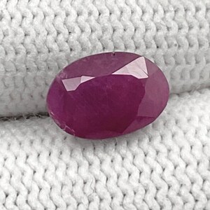 May include: A deep pink oval-shaped gemstone with a faceted cut.