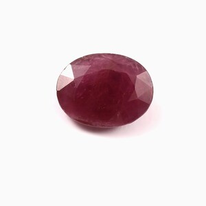 Puede incluir: Una gema de rubí facetada de forma ovalada. La gema es de un color rojo intenso y rico, con múltiples facetas que capturan la luz. El rubí está sobre un fondo blanco liso.