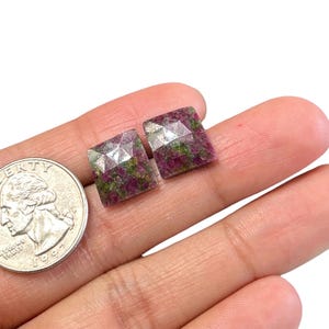 Op de afbeelding: Twee vierkante, gefacetteerde edelstenen met een roze, groene en witte kleurpatroon. De edelstenen zijn ongeveer zo groot als een Nederlandse 2 euro munt.