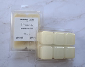 May include: A set of six soy wax melts in a clear plastic container. The melts are a light yellow color and are labeled "Prosperity" with the scent "Bergamot Honey/Musk". The label also includes the text "III John ::2" and "Hand poured Soy wax melt".