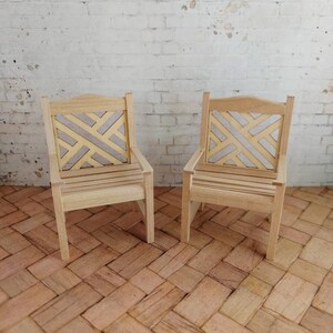 Op de afbeelding: Twee houten stoelen met een geometrisch patroon op de rugleuning. De stoelen zijn gemaakt van lichtbruin hout en hebben een eenvoudig ontwerp.