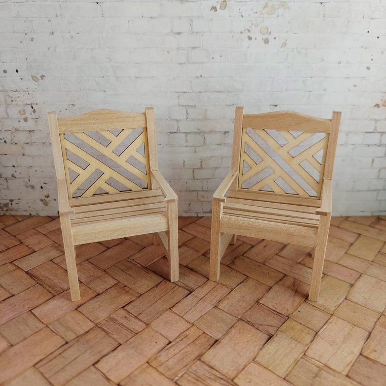 Op de afbeelding: Twee houten stoelen met een geometrisch patroon op de rugleuning. De stoelen zijn gemaakt van lichtbruin hout en hebben een eenvoudig ontwerp.
