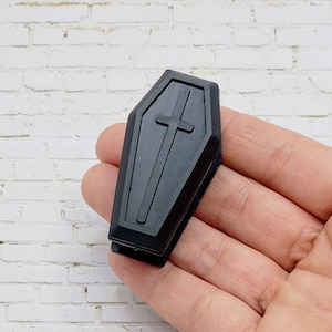 May include: A black plastic coffin-shaped finger puppet with a cross on the front.