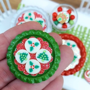 May include: A green bottle cap with a red and white design. The design features four white circles with Christmas tree and holly designs. The bottle cap is perfect for a Christmas craft project.
