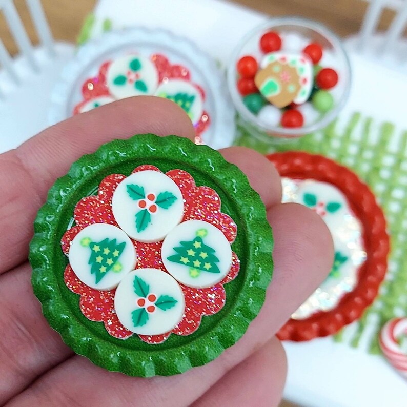 May include: A green bottle cap with a red and white design. The design features four white circles with Christmas tree and holly designs. The bottle cap is perfect for a Christmas craft project.