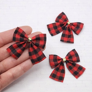 May include: Three red and black buffalo plaid bows with gold accents. The bows are made of fabric and are perfect for adding a touch of holiday cheer to any project.