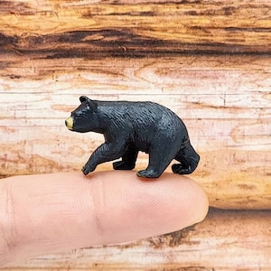 May include: A small black bear figurine, standing on a finger, with a yellow nose.