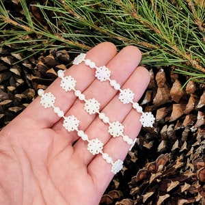 May include: Four strands of white snowflake trim with pearl beads. The trim is made of white lace with a snowflake design. The trim is perfect for adding a touch of elegance to any craft project.