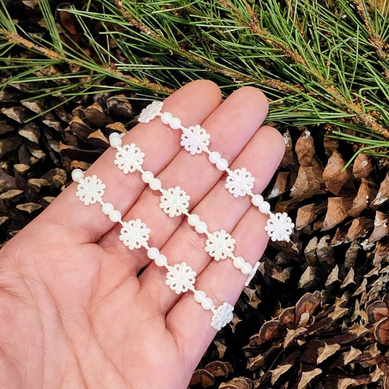 May include: Four strands of white snowflake trim with pearl beads. The trim is made of white lace with a snowflake design. The trim is perfect for adding a touch of elegance to any craft project.