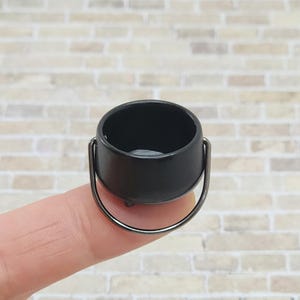 May include: A small black cauldron with a silver handle. The cauldron is about the size of a thimble.