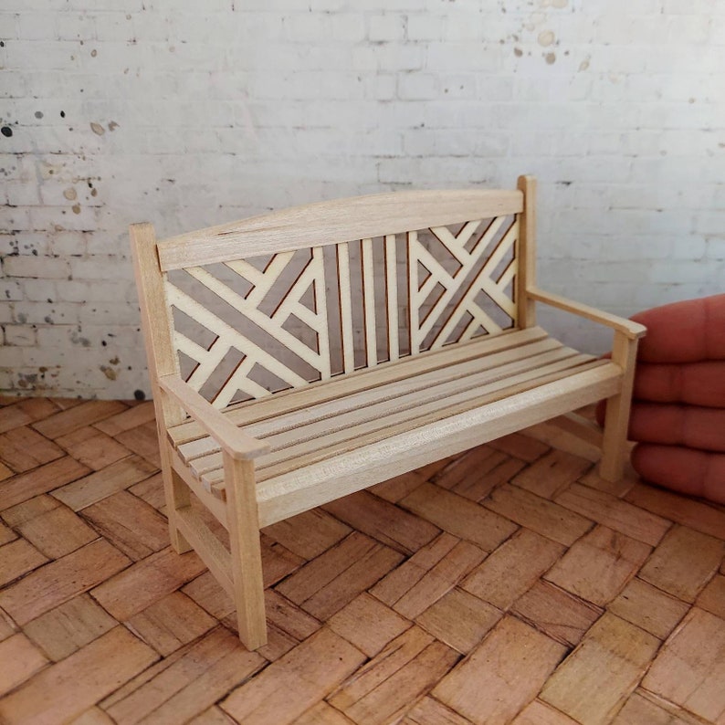 Op de afbeelding: Een houten bank met een geometrisch patroon op de rugleuning. De bank is gemaakt van licht hout en heeft een natuurlijke afwerking.