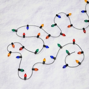 May include: A string of colorful Christmas lights with red, green, blue, orange, and yellow bulbs on a black wire. The lights are arranged in a looping pattern against a white background, creating a festive holiday display.