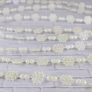 May include: A white garland with iridescent snowflake ornaments and white pearl beads. The garland is perfect for adding a touch of winter magic to your home decor.