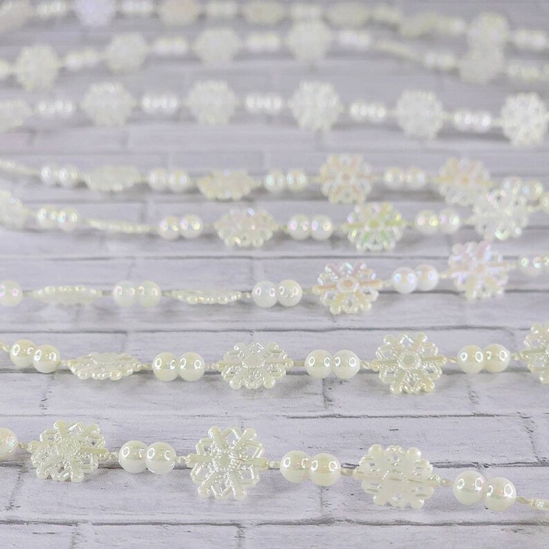 May include: A white garland with iridescent snowflake ornaments and white pearl beads. The garland is perfect for adding a touch of winter magic to your home decor.