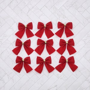 May include: Twelve red velvet bows with gold centres. The bows are arranged in three rows of four.