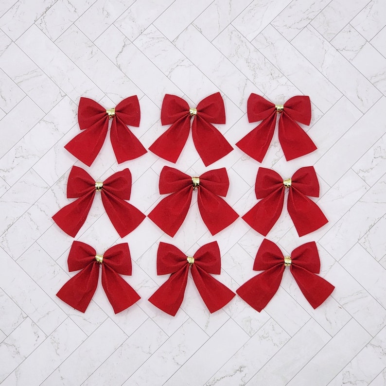 May include: Twelve red velvet bows with gold centres. The bows are arranged in three rows of four.