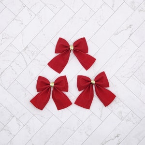 May include: Three red velvet bows with gold centres. The bows are arranged in a triangular pattern on a white marble background.