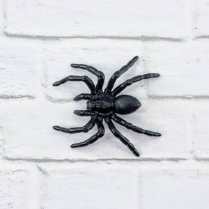 May include: A black plastic spider toy with eight legs. The spider is on a white background.
