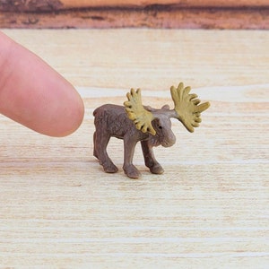 May include: A small, brown plastic moose figurine with large, yellow antlers. The moose is standing on a light wood surface.