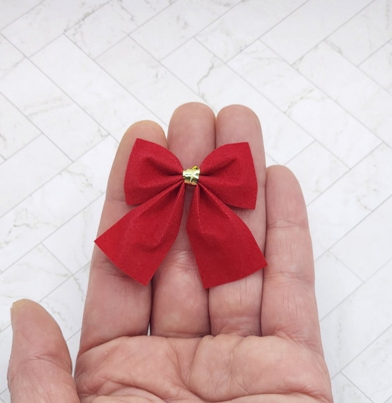 May include: A red velvet bow with a gold centre. The bow is held in a hand.