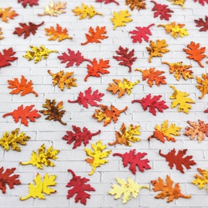 May include: Assortment of fall-themed, paper leaves in various shades of red, orange, and yellow. The leaves are scattered on a white brick background.