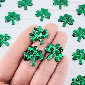 May include: Green shamrock shaped resin embellishments. The shamrocks have a shiny, iridescent finish.