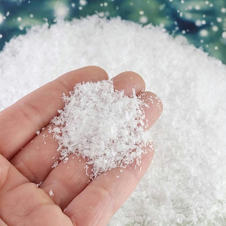 May include: A hand holding a pile of white, fluffy, artificial snow. The snow is made of small, delicate flakes.