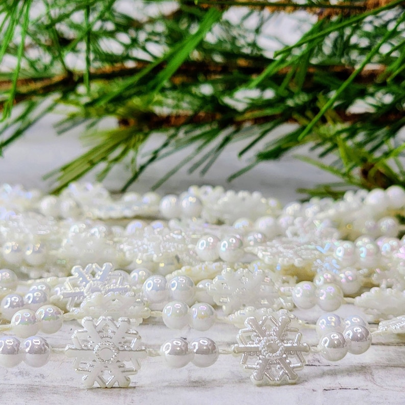 May include: White snowflake garland with iridescent white beads. The garland is made of plastic and is perfect for decorating a Christmas tree or other holiday decor.