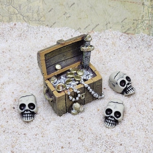May include: A miniature treasure chest filled with gold coins and a pearl necklace, surrounded by three white skulls on a sandy surface.