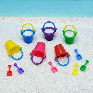 May include: A collection of colorful miniature beach toys, including buckets and shovels. The buckets are in various colors: yellow, blue, purple, pink, red, and green. The shovels are in red, purple, pink, yellow, and green. The toys are on a white sandy surface.