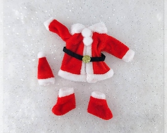 May include: A red and white Santa Claus costume for a doll. The costume includes a jacket, pants, and a hat. The jacket has a black belt with a gold buckle.