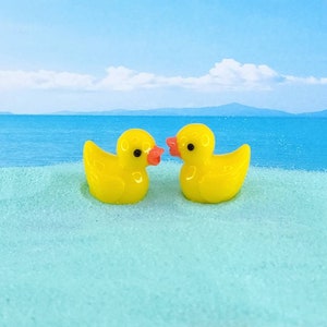 May include: Two yellow rubber duck figurines facing each other on a light blue surface. The ducks have orange beaks and are made of a glossy material.