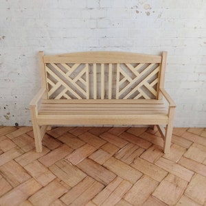 Op de afbeelding: Een houten bank met een geometrisch patroon op de rugleuning en een zitting met latten. De bank is lichtbruin en staat op een houten vloer.