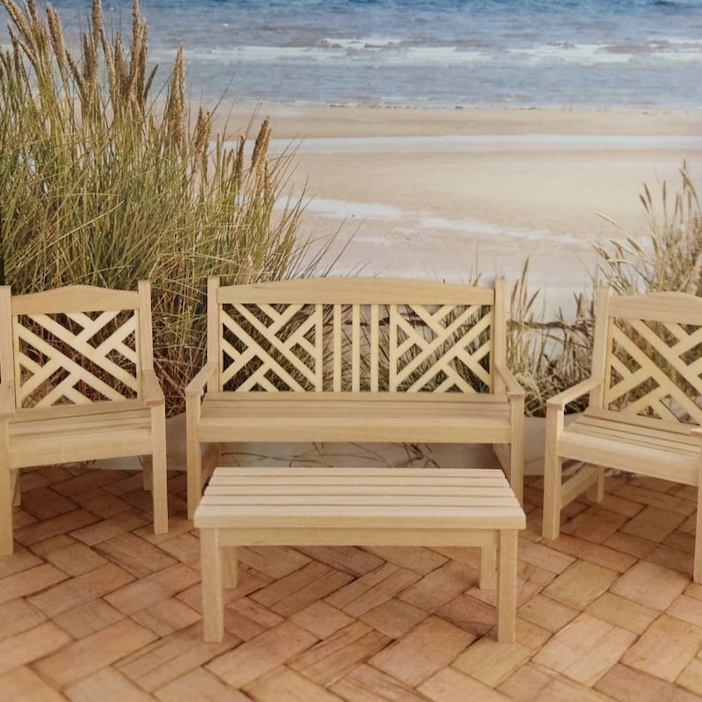 Op de afbeelding: Een set van drie houten tuinstoelen met een tralieontwerp. De stoelen zijn in een rij geplaatst met een kleine houten tafel ervoor. De stoelen en de tafel zijn allemaal gemaakt van natuurlijk hout en hebben een lichtbruine afwerking.