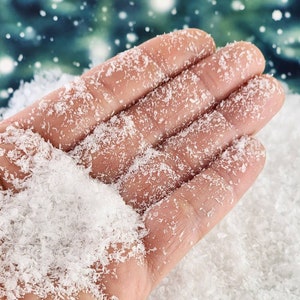 May include: A hand covered in white, fluffy fake snow. The snow is loose and resembles a light, powdery snow.